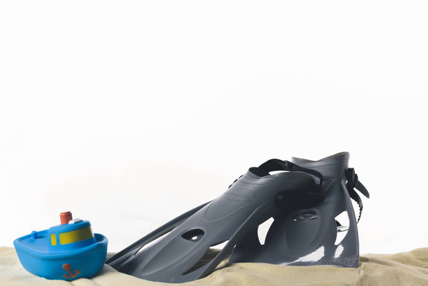 Flippers en speelgoed boot in zand geïsoleerd op wit - Foto, afbeelding
