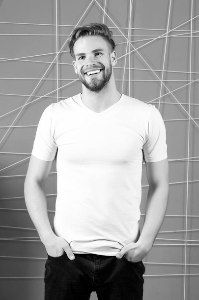 Bearded man smile in white tshirt and jeans. Happy macho with beard on unshaven face. Guy smiling with blond hair and stylish haircut. Hair care in salon or barbershop. Mens beauty and fashion - Zdjęcie, obraz