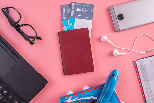 Flugzeug, Flugtickets, Reisepass, Notizbuch und Telefon mit Kopfhörer auf rosa Hintergrund. die Aussicht von oben. das Konzept der Planung und Vorbereitung der Reise - Foto, Bild