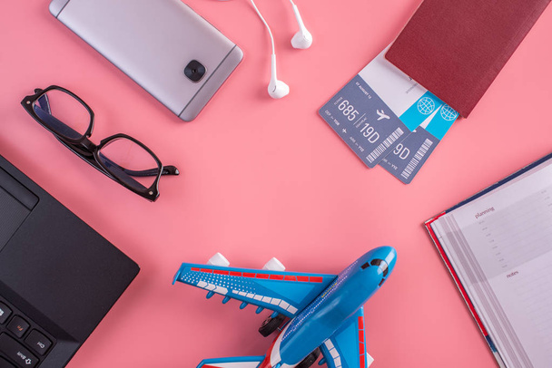 Avión, billetes de avión, pasaporte, cuaderno y teléfono con auriculares sobre fondo rosa. La vista desde arriba. El concepto de planificación y preparación para el viaje
 - Foto, Imagen