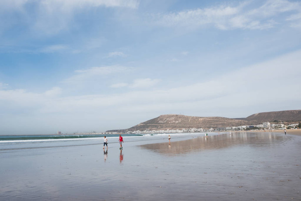 Foto van onherkenbaar mensen lopen aan zandstrand met blauwe lucht - Foto, afbeelding
