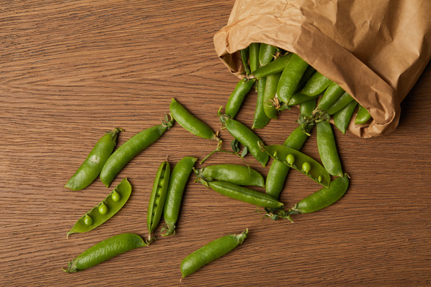 top view of pea pods spilled from paper bag on wooden table - Foto, imagen