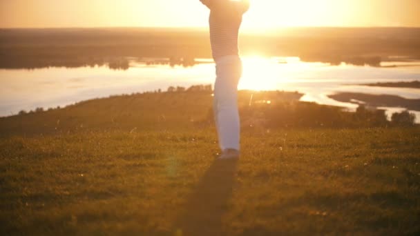 Erkek siluet ahşap bir günlük çimenlerin üzerinde yaz gün batımında tepede atar - Video, Çekim