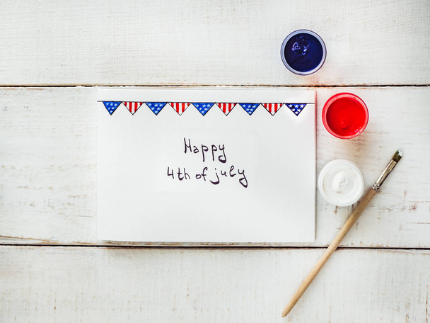 Card with a pattern of the US Flag, handwritten inscription with congratulations on July 4th on a white, vintage, wooden table. Top view, close-up. Concept of an independent, strong country and nation - Photo, image