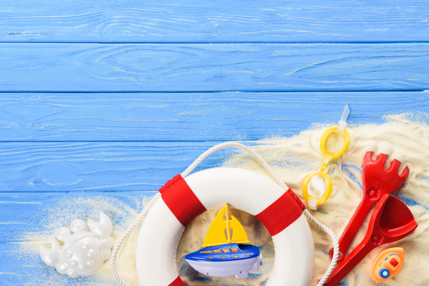 Anillo salvavidas y barcos de juguete sobre fondo de madera azul
 - Foto, Imagen
