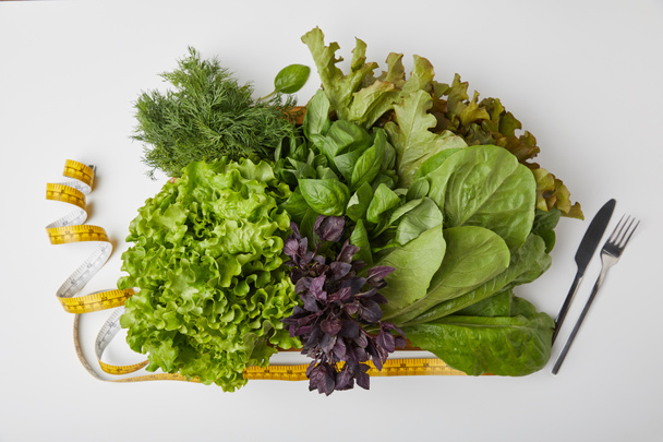 вид сверху на различные спелые овощи в коробке со столовыми приборами и измерительной лентой на белой поверхности
 - Фото, изображение