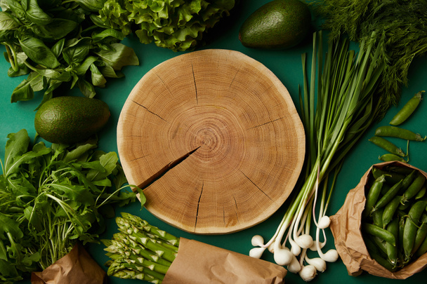 top view of wood cut surrounded with various ripe vegetables on green surface - Foto, Imagem