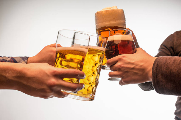 hands with mugs of beer toasting creating splash isolated on white background - Zdjęcie, obraz