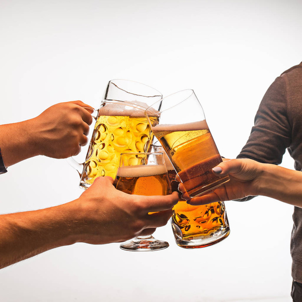 hands with mugs of beer toasting creating splash isolated on white background - Photo, image