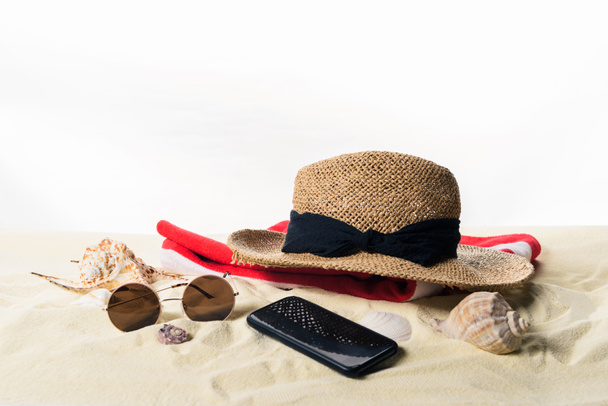 Sombrero de paja sobre toalla y gafas de sol con conchas marinas en arena aislada sobre blanco
 - Foto, Imagen