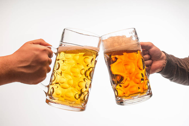 hands with mugs of beer toasting creating splash isolated on white background - Photo, Image