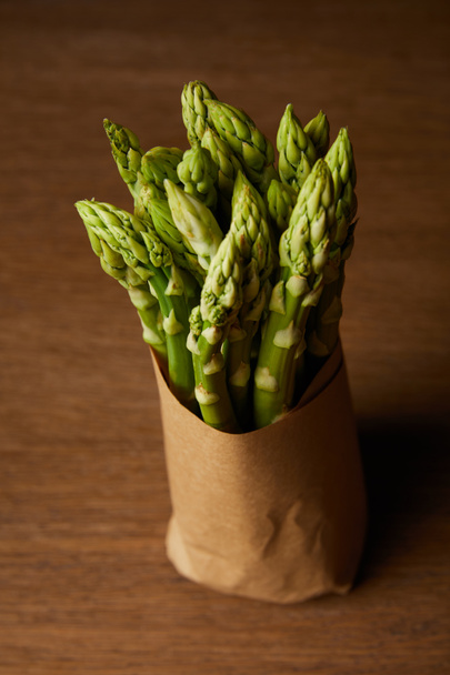 close-up shot of bunch of asparagus covered with kraft paper on wooden surface - Fotó, kép