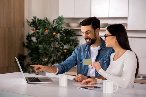 Financial advisor. Cheerful young couple using online banking while sitting in the kitchen - Foto, Imagem