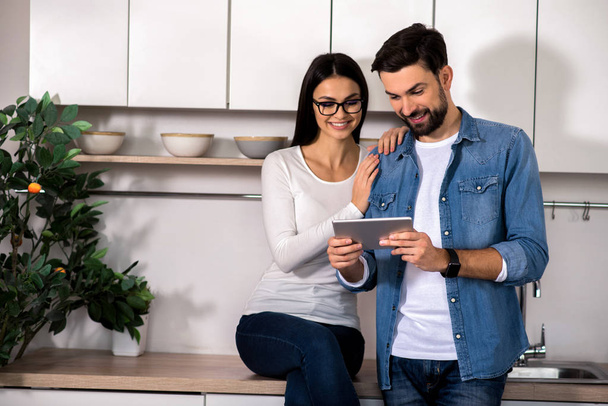 Modern device. Cheerful young couple resting together in the kitchen while using their laptop - Foto, Bild