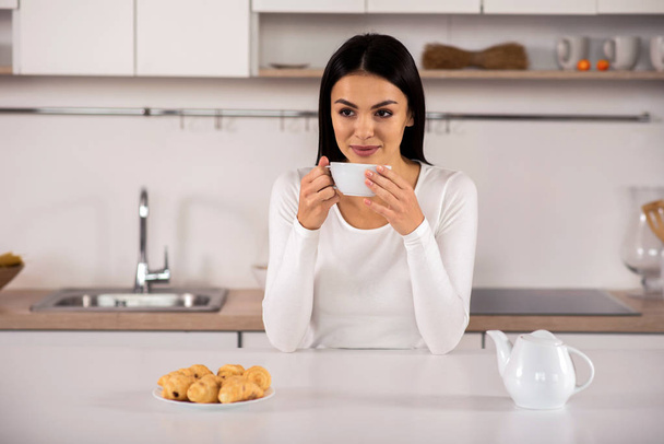 Απολαύστε τη γεύση. Χαρά ελκυστική γυναίκα πίνοντας τσάι ενώ ξεκουραζόταν στην κουζίνα - Φωτογραφία, εικόνα