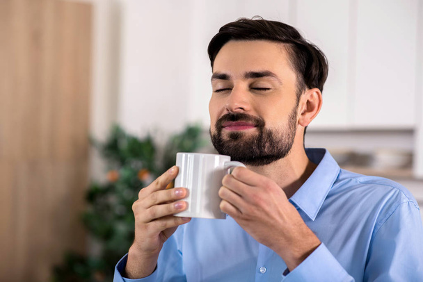 Just enjoy. Cheerful handsome businessman smelling his coffee in the kitchen - Foto, Imagem