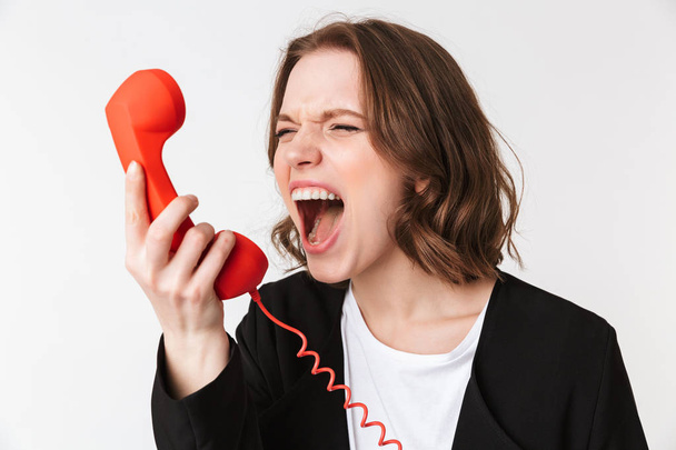 Image of screaming agressive young woman standing isolated talking by telephone looking aside. - Фото, зображення