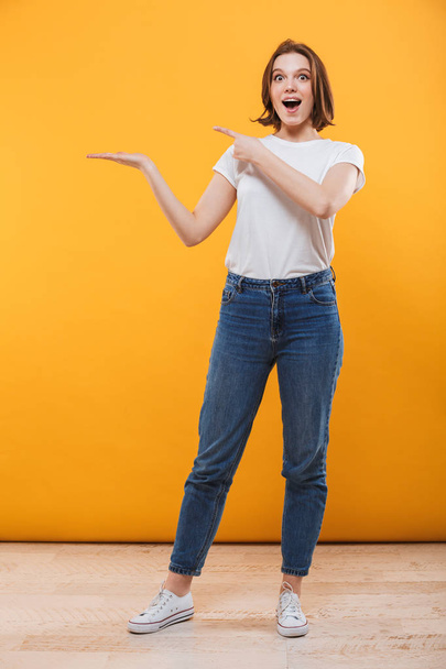 Image of excited emotional young woman standing isolated over yellow background showing copyspace. - Foto, afbeelding