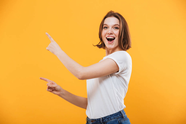 Image of excited emotional young woman standing isolated over yellow background showing copyspace. - Photo, image