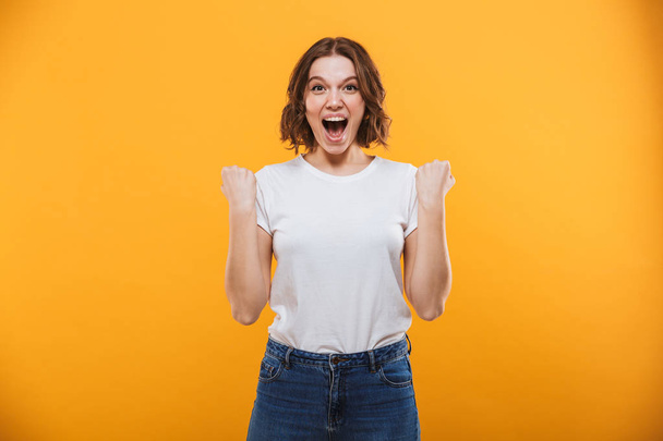 Image of excited young woman standing isolated over yellow background looking camera make winner gesture. - Foto, Bild