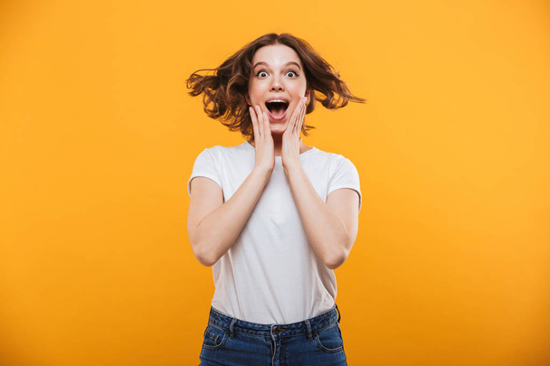 Image of shocked young woman standing isolated over yellow background looking camera. - Фото, изображение