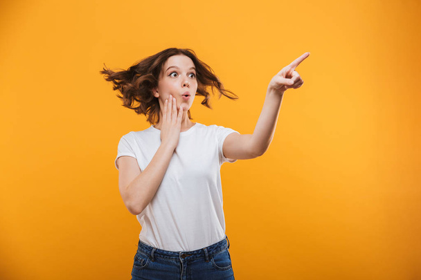 Image of excited young woman standing isolated over yellow background showing copyspace looking aside. - Fotografie, Obrázek