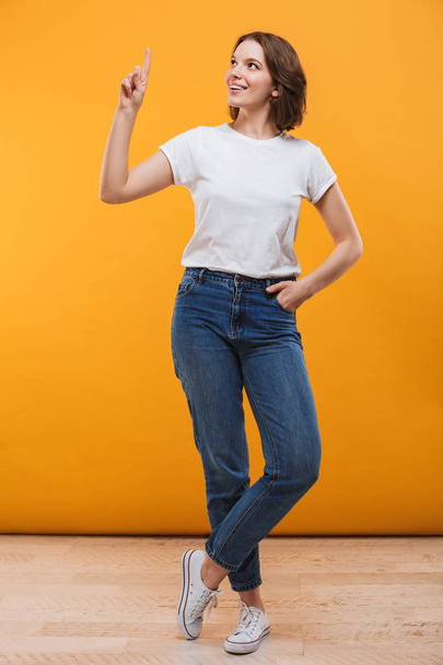 Image of excited young woman standing isolated over yellow background showing copyspace looking aside. - Фото, изображение