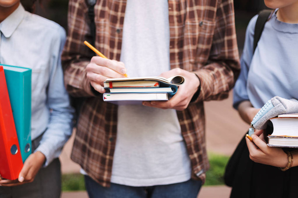 Close up photo of young man holding pencil and books in hands - Фото, изображение