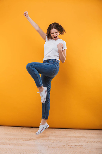 Photo of emotional young woman jumping isolated over yellow background make winner gesture. - Foto, Imagem