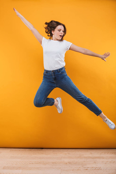 Photo of excited young woman jumping isolated over yellow background. - Fotó, kép