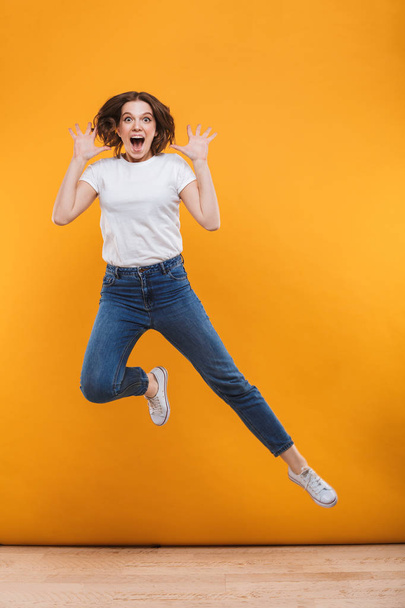 Photo of emotional young woman jumping isolated over yellow background. Looking camera. - Foto, Imagem