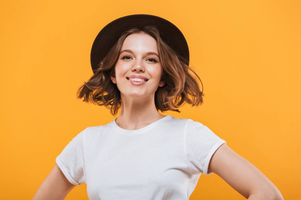 Image of cheerful wearing hat young woman standing isolated over yellow background looking camera. - Photo, image
