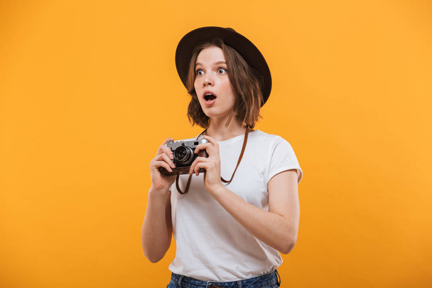 Image of excited emotional young woman photographer tourist standing isolated over yellow background holding camera. - Zdjęcie, obraz