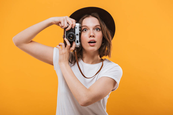 Image of excited emotional young woman photographer tourist standing isolated over yellow background holding camera. - Foto, Bild