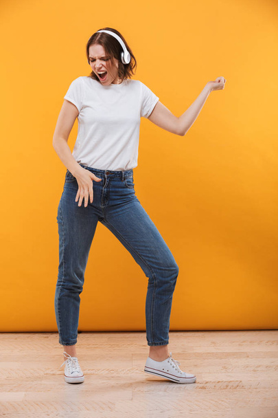 Image of emotional funny young woman standing isolated over yellow background listening music singing. - Fotoğraf, Görsel
