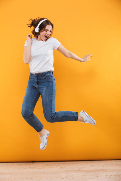 Image of emotional funny young woman jumping isolated over yellow background listening music. - Fotoğraf, Görsel