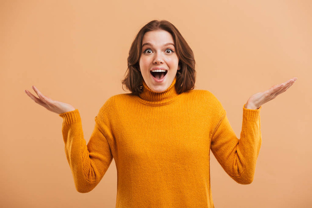 Portrait of an excited young woman in sweater gesturing with hands over beige background - Photo, Image