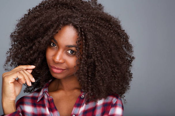 Крупный план портрета стильной молодой африканской женщины с вьющимися волосами на сером фоне
 - Фото, изображение