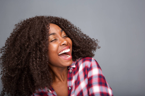 Крупный план портрета веселой молодой африканской женщины, смеющейся на сером фоне
 - Фото, изображение