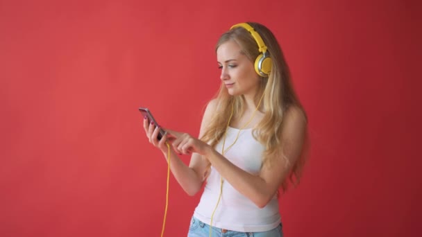 Young pretty caucasian woman holding mobile phone and listening music with earphones over red background - Video
