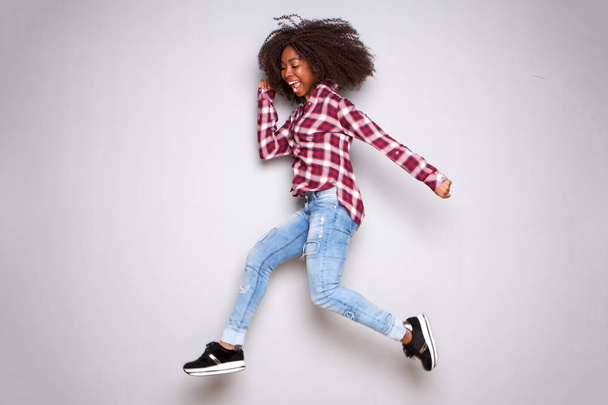 Ganzkörperporträt einer glücklichen jungen Afrikanerin, die über weißen Hintergrund springt - Foto, Bild