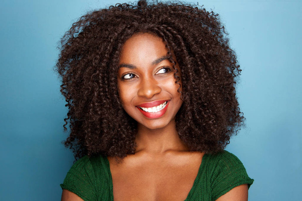 Primer plano retrato de la atractiva joven africana con el pelo rizado mirando hacia otro lado sobre fondo azul
 - Foto, Imagen