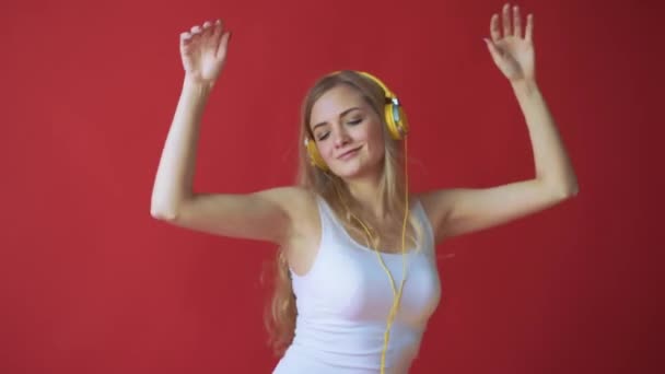 Young pretty caucasian woman holding mobile phone and listening music with earphones over red background - Footage, Video