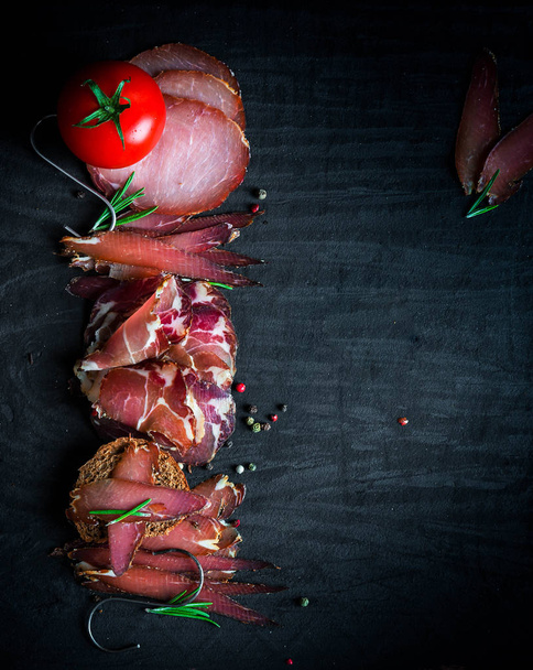 A set of different types of raw smoked meat. Jamon Lomo, oppa and fillet on a black background.  - Fotoğraf, Görsel