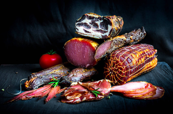 A set of different types of raw smoked meat. Jamon Lomo, oppa and fillet on a black background.  - Foto, Bild