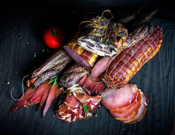 Een verzameling van verschillende soorten rauwe gerookt vlees. Jamon Lomo, oppa en filet op een zwarte achtergrond.  - Foto, afbeelding