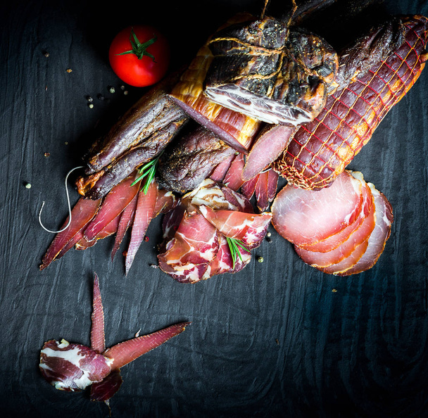A set of different types of raw smoked meat. Jamon Lomo, oppa and fillet on a black background.  - Φωτογραφία, εικόνα