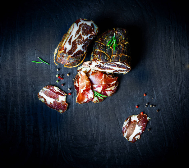 A set of different types of raw smoked meat. Jamon Lomo, oppa and fillet on a black background.  - Foto, imagen