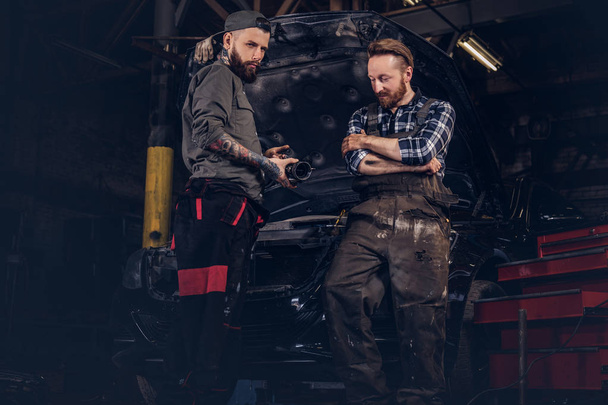 Twee monteur te praten tijdens herstelt een gebroken auto in een garage. - Foto, afbeelding
