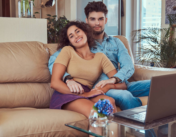glückliches attraktives Paar während eines Wochenendes, Film auf dem Laptop sitzend auf dem Sofa zu Hause. - Foto, Bild